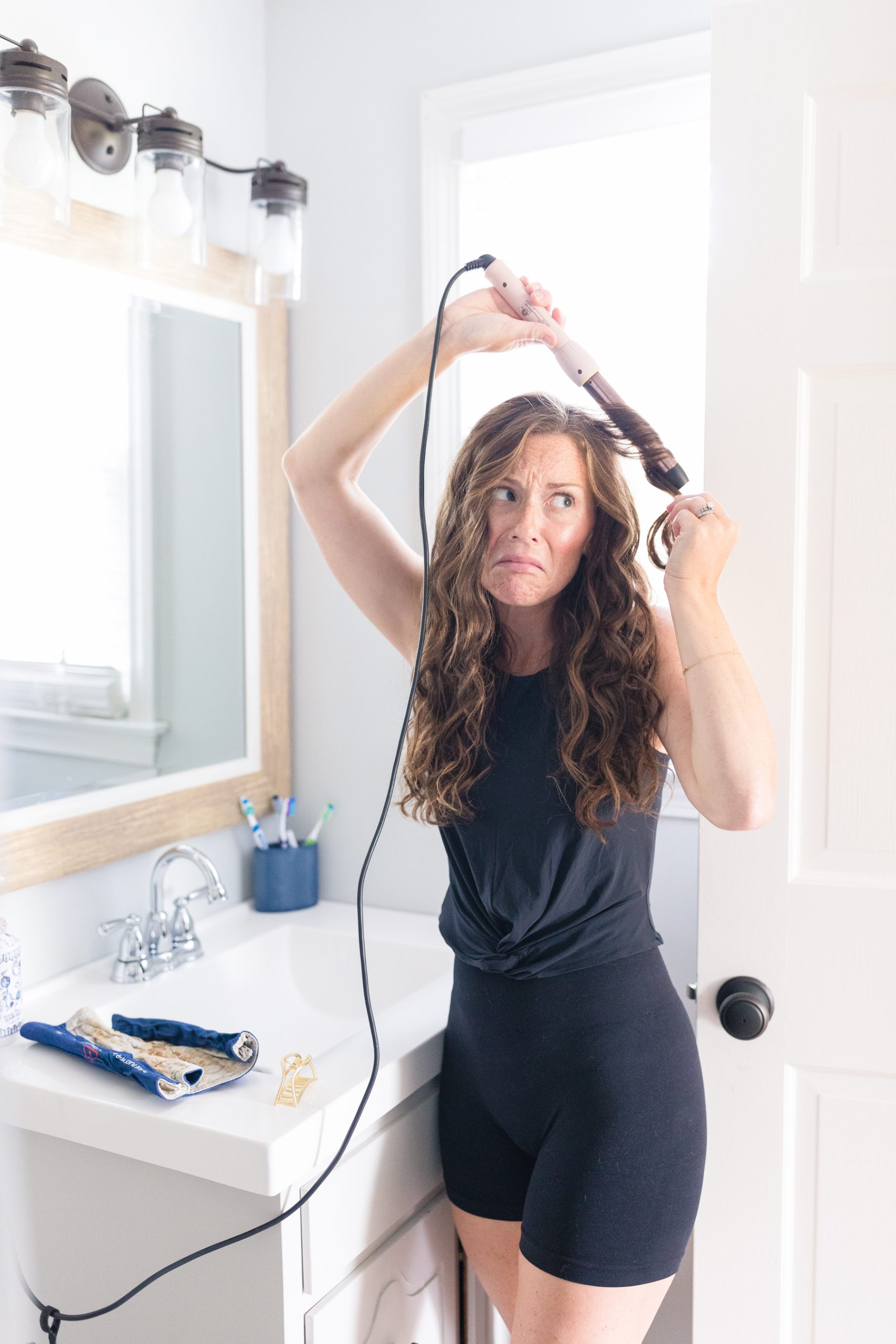 woman making funny face while curling her hair with a wand