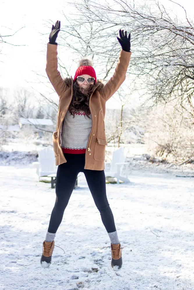 girl wearing winter clothes jumping in the air in the snow