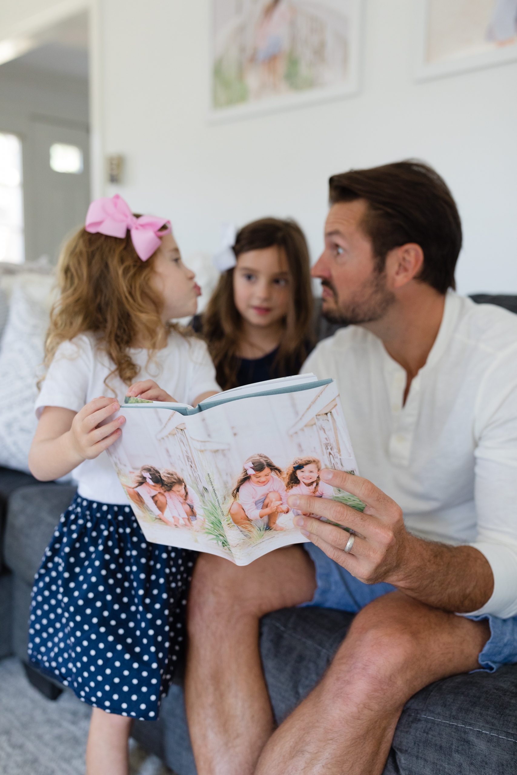 little girl sticking tongue out at dad holding a photo book